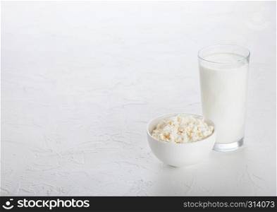 Glass of milk and bowl of cottage cheese on white stone kitchen table background.