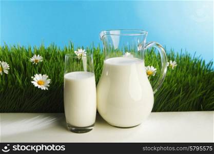 Glass of milk and jar on fresh grass meadow with chamomiles. Glass of milk and jar on flower meadow
