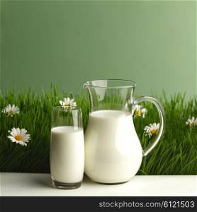 Glass of milk and jar on fresh grass meadow with chamomiles