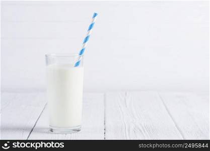 Glass of milk with paper striped straw on white wooden table still life with copy space