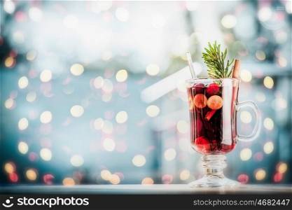 Glass of mulled wine with berries and fir branch on table at frosty winter day background with festive bokeh lighting background.