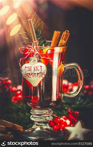 Glass of mulled wine with festive decoration and text Merry Christmas at bokeh background, front view