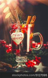Glass of mulled wine with festive decoration and text Merry Christmas at bokeh background, front view