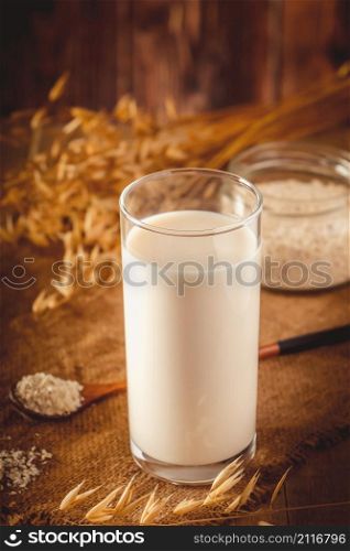 Glass of oat milk on a wooden background. Lactose-free vegetable diet milk. Gluten free oat drink on a brown wooden background. Super Food - A glass of oat milk for a healthy diet. Trending food, vertical photo. Place for your text.. Glass of oat milk on a wooden background.