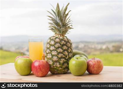 glass of orange juice and lots of fruits on wooden table outdoor