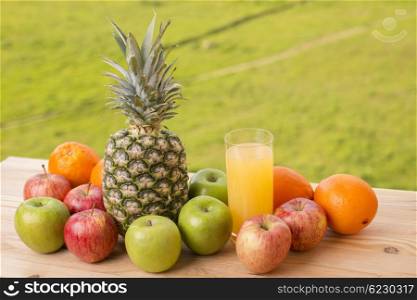 glass of orange juice and lots of fruits on wooden table outdoor
