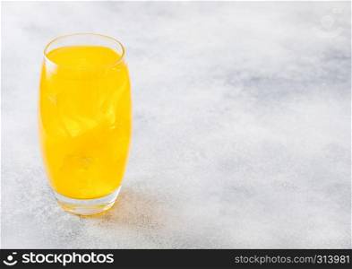 Glass of orange soda drink with ice cubes and bubbles on stone kitchen background.