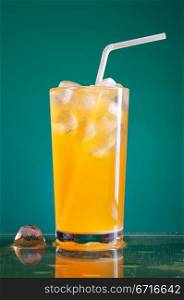 glass of orange soda with ice and straw over blue background