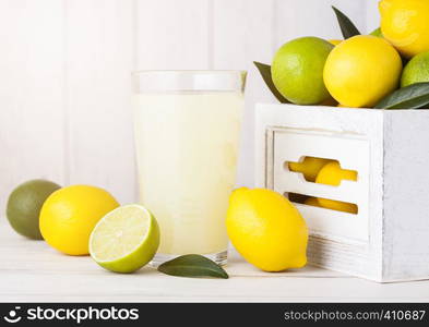 Glass of organic fresh lemon and lime juice with raw lemons and limes in white wooden box