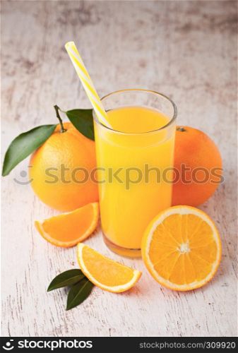 Glass of organic fresh orange juice with raw oranges on light wooden background