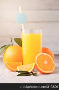 Glass of organic fresh orange juice with raw oranges on light wooden background