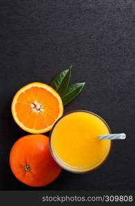 Glass of organic fresh orange smoothie juice with raw oranges on black wooden background.Top view