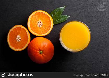 Glass of organic fresh orange smoothie juice with raw oranges on black wooden background.Top view