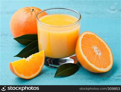 Glass of organic fresh orange smoothie juice with raw oranges on blue wooden background.