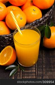 Glass of organic fresh orange smoothie juice with raw oranges on dark wooden background