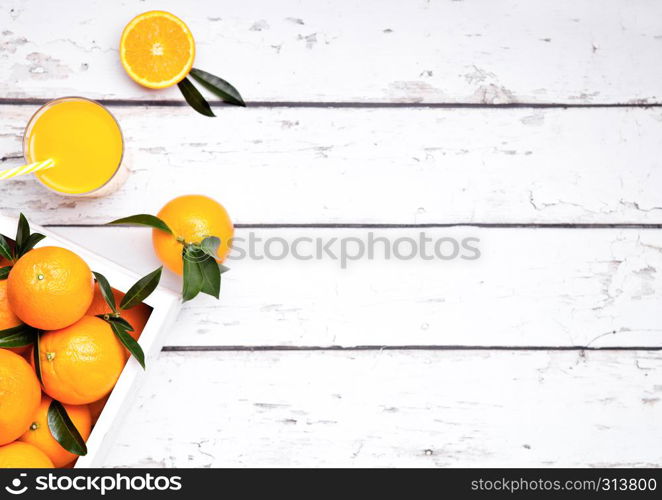 Glass of organic fresh orange smoothie juice with raw oranges on light wooden background in white wooden box.Top view.