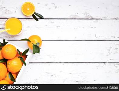 Glass of organic fresh orange smoothie juice with raw oranges on light wooden background in white wooden box.Top view.