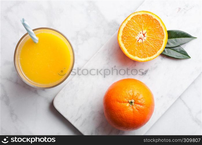 Glass of organic fresh orange smoothie juice with raw oranges on white marble background.Top view