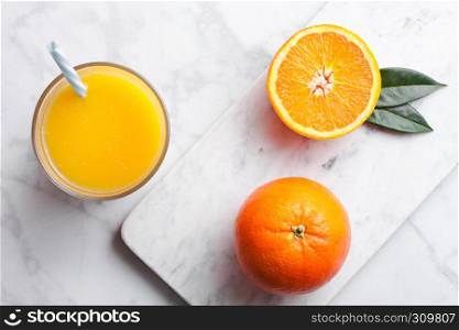 Glass of organic fresh orange smoothie juice with raw oranges on white marble background.Top view