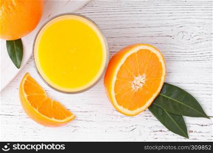 Glass of organic fresh orange smoothie juice with raw oranges on white wooden background.Top view