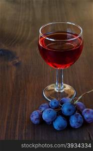 Glass of red wine and a cluster of grapes on dark wooden board