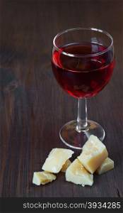 Glass of red wine and a piece of Parmesan cheese on dark wooden board