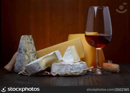 Glass of red wine and cheese assortment on wooden table still life
