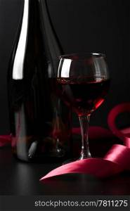glass of red wine and red ribbon over black background