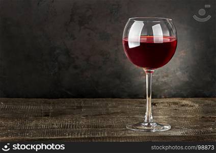 Glass of red wine on a wooden table. Dark blurry background.