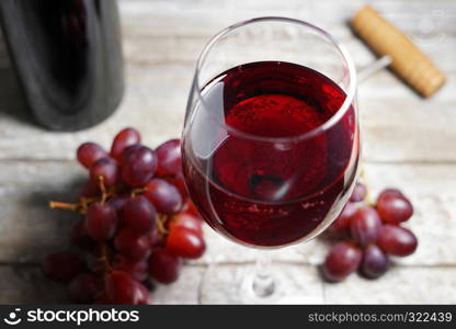 Glass of red wine on a wooden table in a rustic and vintage wine bar with grapes fruit and a bottle of wine on background closeup view.