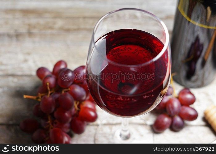 Glass of red wine on a wooden table in a rustic and vintage wine bar with grapes fruit and a bottle of wine on background close up view.