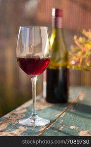 Glass of red wine on an old, rustic wood table. Enjoying it in the own garden in the evening sun.