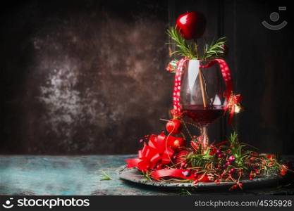 Glass of red wine on rustic table with festive Christmas decoration and rosemary at dark wooden background, side view, place for text