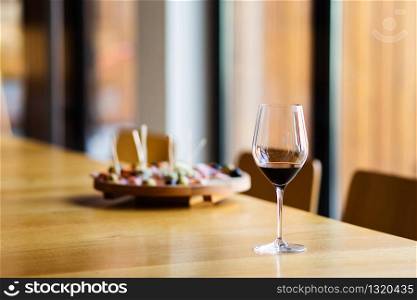 Glass of red wine on the table at home or restaurant in front of the defocused blur appetizer by the window