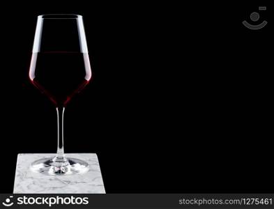 Glass of red wine on white marble board on black background.