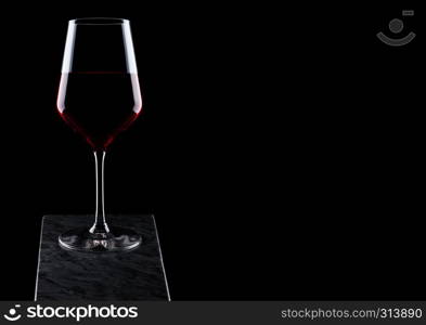 Glass of red wine on wooden board on black background.