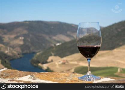 Glass of red wine or port for tasting above the hillsides of the Douro valley in Portugal. Glass of red wine above the valley of the River Douro in Portugal