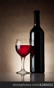 Glass of red wine with a bottle on burlap background