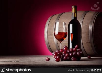 Glass of red wine with bottle and grapes on red background. Glass of red wine with bottle and grapes