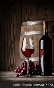 Glass of red wine with bottle and keg standing on a wooden background. Glass of red wine with bottle and keg standing
