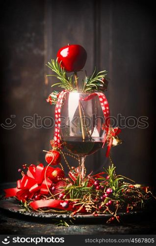Glass of red wine with Christmas decorations and rosemary branches on table at dark wooden background, side view