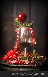 Glass of red wine with Christmas decorations and rosemary branches on table at dark wooden background, side view