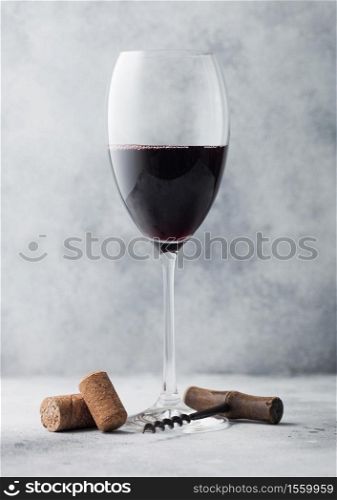 Glass of red wine with corks and opener on light table background.