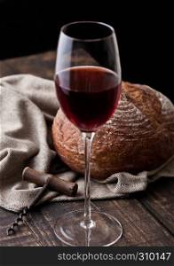 Glass of red wine with fresh loaf of bread with retro corkscrew in kitchen on wooden table