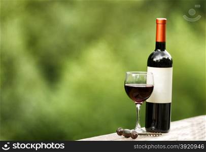 Glass of red wine with full bottle and corkscrew on rustic wood outdoors. Selective focus on front of wine glass with shallow depth of field on horizontal layout.