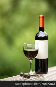 Glass of red wine with full bottle and corkscrew on rustic wood outdoors. Selective focus on front of wine glass with shallow depth of field on vertical layout.