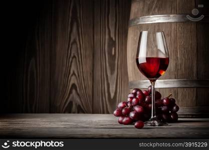 Glass of red wine with grapes and barrel on the background of wooden wall. Glass of red wine with grapes and barrel