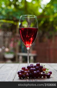 Glass of red wine with grapes on table in park. Romantic lunch