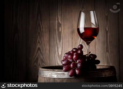 Glass of red wine with grapes on wooden barrel at the wooden wall. Glass of red wine with grapes on wooden barrel