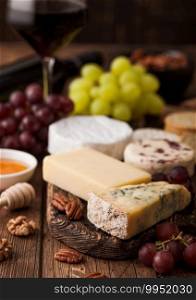Glass of red wine with selection of various cheese and grapes on wooden table background. Blue Stilton, Red Leicester and Brie Cheese and knife with honey.